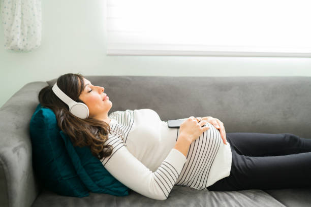 mère enceinte dormant avec la musique sur le divan - lying on side audio photos et images de collection