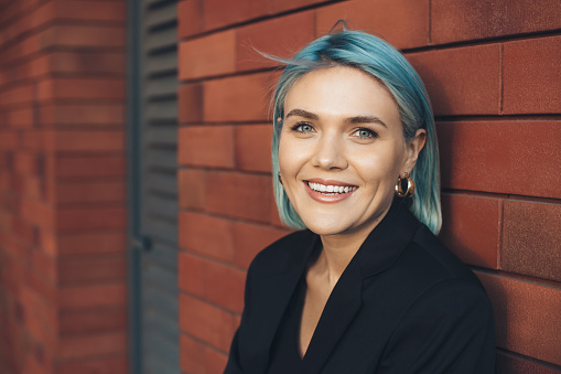 Blue haired woman posing on a brick wall outside smile at camera in a business suit