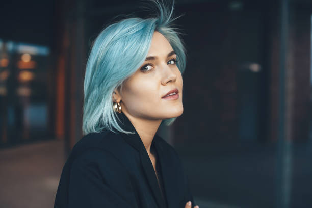 młoda urocza dama z niebieskimi włosami pozująca na zewnątrz i patrząca na kamerę z budynkiem na tle - blue hair zdjęcia i obrazy z banku zdjęć