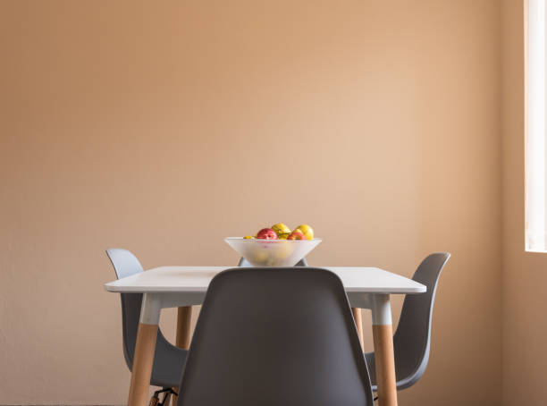 istock Small white table with fruit bowl and grey chairs against peach wall 1301520491