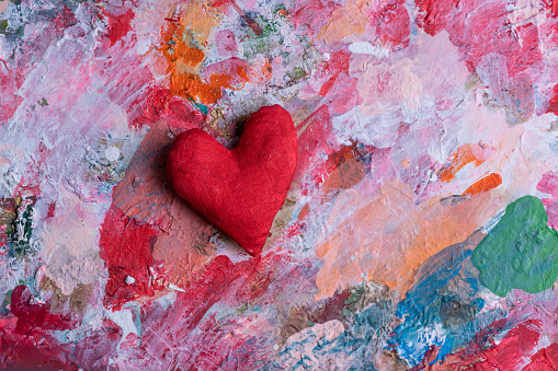 Homemade rag heart against the background of multi-colored shades of paint on the artist's palette
