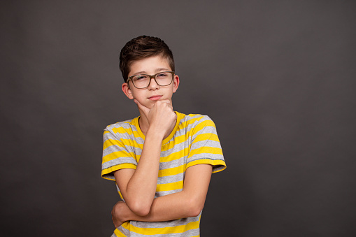 a boy with glasses looks thoughtfully into the distance on a dark gray background. High quality photo