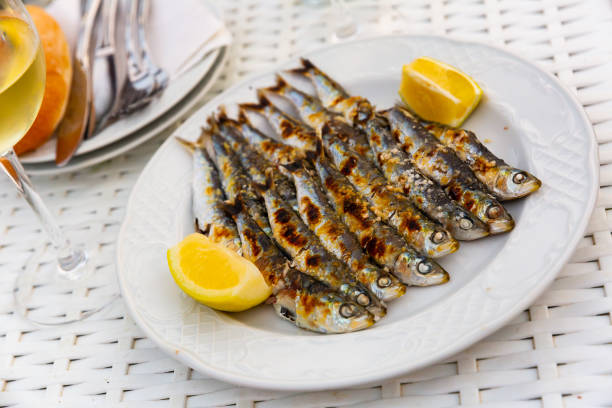 Malaga cuisine grilled sardines served with lemon on white plate on wooden table