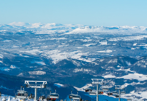 Panoramic view over a ski resort with people in chair lifts and majestic mountains in the background.