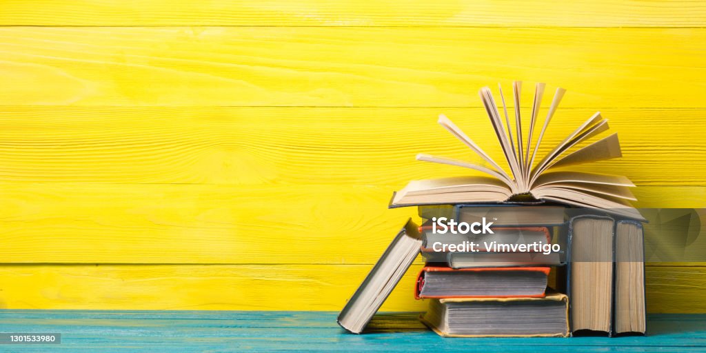 Books on bookshelf in Library. Back to School education concept on colored abstract yellow background. Open hardback book stack in a raw on wooden desk table. Books on shelf. Vintage old hardback tall book stacking heap, open fanned pages on wooden deck desk table and abstract yellow background. Back to school. Copy Space for ad text. Education knowledge Library Law concept Book Stock Photo