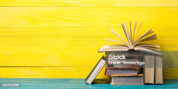 Books On Bookshelf In Library Back To School Education Concept On Colored Abstract Yellow Background Open Hardback Book Stack In A Raw On Wooden Desk Table Stock Photo - Download Image Now