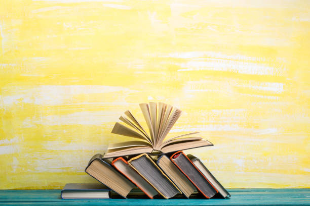 istock Books on bookshelf in Library. Back to School education concept on colored abstract yellow background. Open hardback book stack in a raw on wooden desk table. 1301534080