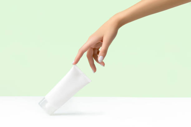 istock Womans hand holding white tube on pastel green background 1301536020