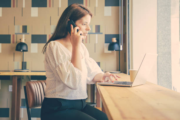 istock Focused brunette woman using laptop and talking on smartphone 1301538779