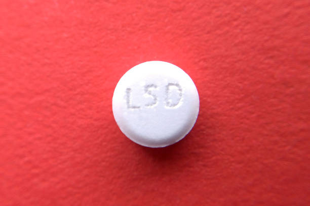 tableta lsd sobre fondo borroso rojo - lsd fotografías e imágenes de stock