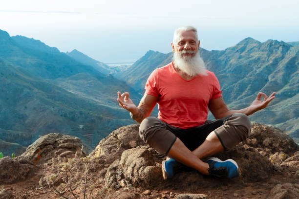 Senior man greeting sunset Senior athlete man with white beard and tattoo greeting sunrise and meditating, mindful living and healthy wellbeing concept man yoga tattoo stock pictures, royalty-free photos & images
