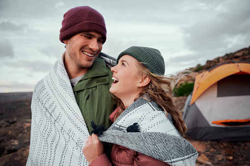 Laughing young romantic couple in a blanket standing together on mountain looking at each other