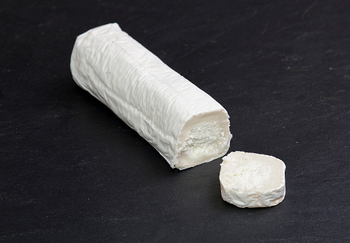 Goat cheese roller with slice. Isolated over black slate