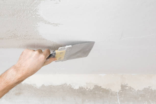 istock Young adult man hand using spatula and plastering ceiling with white fresh finishing putty. Closeup. Repair work of home. View from below. 1301544490