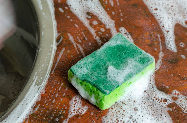 istock Green foam dish sponge. Sponge on the red kitchen table next to the sink. 1301545433