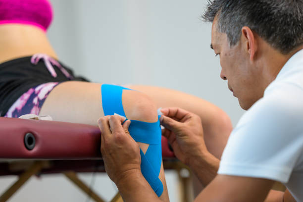 fisioterapeuta masculino aplicando fita de kinesio azul no joelho da mulher - 2498 - fotografias e filmes do acervo
