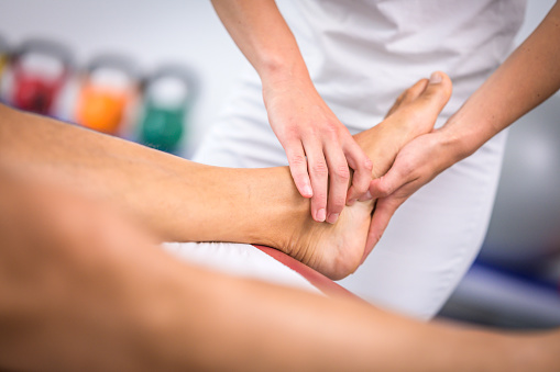 Close-up of female physiotherapist massaging male patient's foot in her clinic.