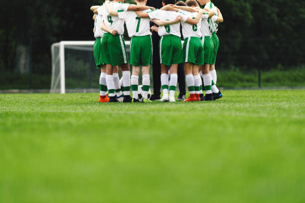 club de fútbol juvenil. chicos acurrucados en el equipo de fútbol. entrenador deportivo del equipo dando discurso previo al juego a los adolescentes del grupo de la escuela. - soccer child coach childhood fotografías e imágenes de stock