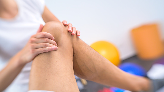 Close-up of female physiotherapist massaging male patient's knee in her clinic.