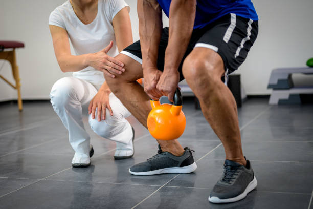 Man exercising with yellow kettlebell Low section of female physiotherapist helping mature man while exercising with yellow kettlebell in clinic. checking sports stock pictures, royalty-free photos & images