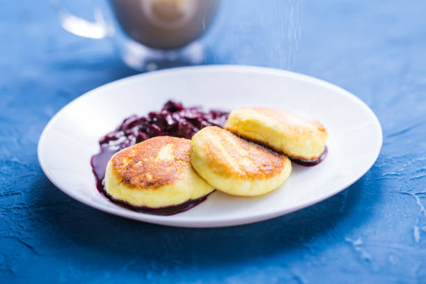 frühstück und leckeres konzept - pfannkuchen aus hüttenkäse mit marmelade, blauem hintergrund. mit puderzucker bestreuen. - cheesecake syrup cottage cheese cream stock-fotos und bilder