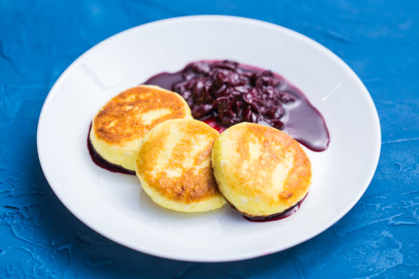 frühstück und leckeres konzept - pfannkuchen aus hüttenkäse mit marmelade, blauem hintergrund. - cheesecake syrup cottage cheese cream stock-fotos und bilder