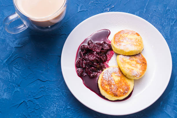 frühstück und leckeres konzept - pfannkuchen aus hüttenkäse mit marmelade, blauem hintergrund, ansicht von oben - cheesecake syrup cottage cheese cream stock-fotos und bilder