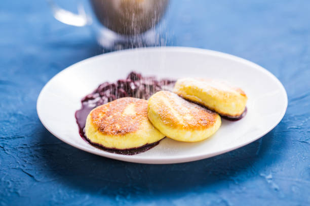 frühstück und leckeres konzept - pfannkuchen aus hüttenkäse mit marmelade, blauem hintergrund. mit puderzucker bestreuen. - cheesecake syrup cottage cheese cream stock-fotos und bilder