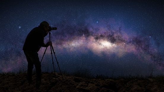 Silhouette of a photographer shooting the milky way in a starry night sky.