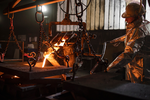Proceso de fundición de acero en fundición. Trabajador con traje protector vertiendo acero fundido en moldes. photo
