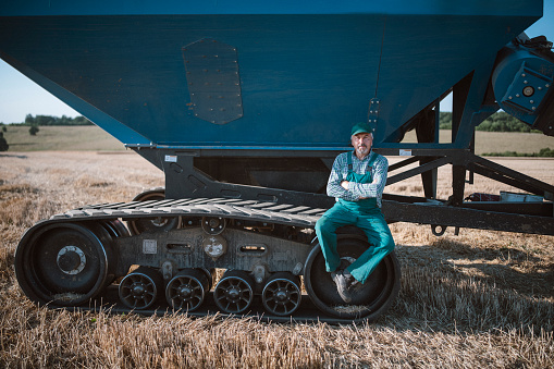 Portrait of a senior farmer taking a break, sitting on the trailer and looking at camera.