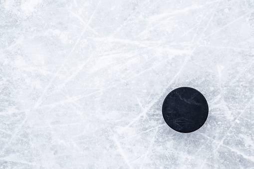 Black old rubber puck on ice background. Closeup. Empty place for text. Top down view.