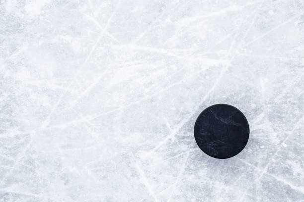 Black old rubber puck on ice background. Closeup. Empty place for text. Top down view. stock photo