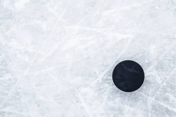Photo of Black old rubber puck on ice background. Closeup. Empty place for text. Top down view.