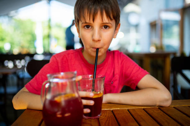 istock Boy sitting at the table and drinking cold red juice through a straw 1301550693