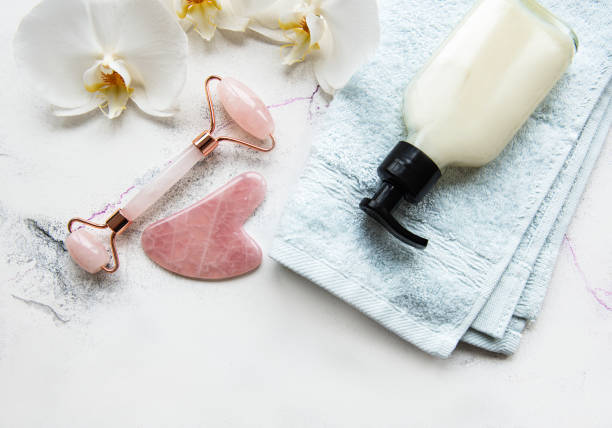 istock Face massage jade roller with cosmetic product on white marble background 1301555156