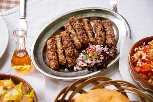 Ground beef kebabs, ten pieces serving with chopped onion on oval steel plate on restaurant table