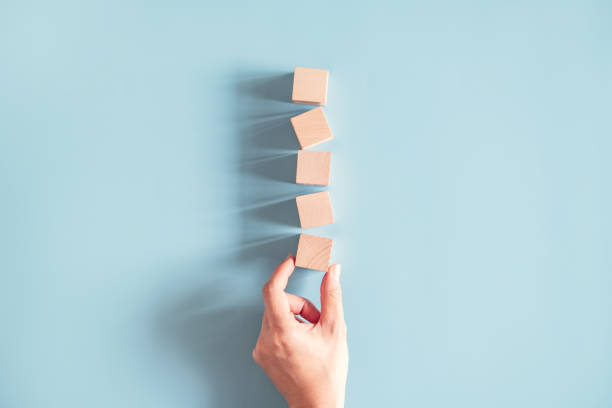 Hand arranging empty wood cube stacking on blue paper background. Space for symbol.