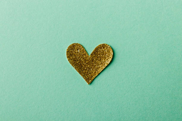 autocollant doré brillant de forme de coeur sur le fond vert - glister photos et images de collection