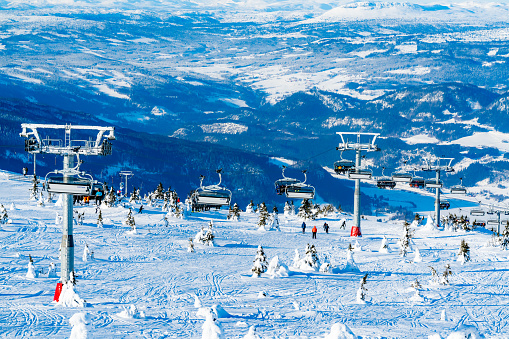 Panoramic view over a ski resort with people in chair lifts and majestic mountains in the background. High quality photo