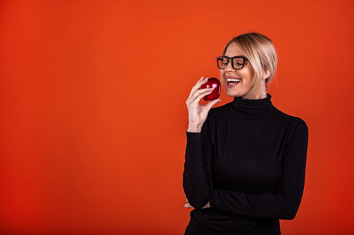 Cropped studio portrait of a happy young woman holding red apple against a red background.