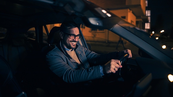 Happy charming man driving his modern car at night