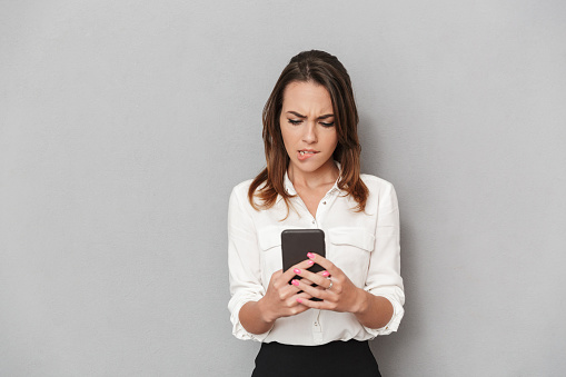 Portrait of a frustrated young business woman using mobile phone isolated over white background