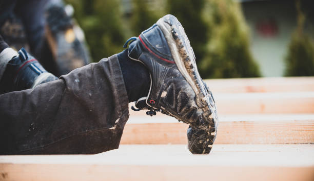 Detailed view of a sturdy black leather work boot with laces on textured pavement, highlighting durability and style. Ideal for themes like workwear, fashion, and outdoor activities.