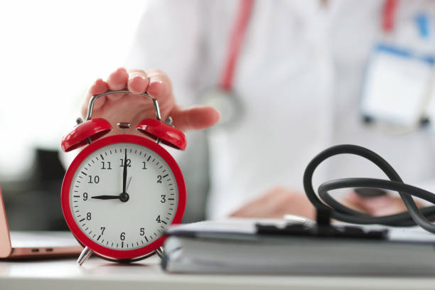 istock Doctors hand turning on red alarm clock in office closeup 1301570877