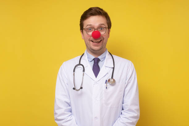 funny caucasian doctor with clown red nose smiling at camera - clowns nose imagens e fotografias de stock