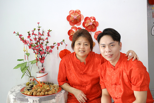 An Asian mother and son in traditional clothing is feeling cheerful for Chinese New Year celebration at home.