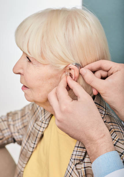 istock Audiologist inserting hearing aid on a senior woman's ear, close-up. Deafness treatment, hearing solution 1301574035