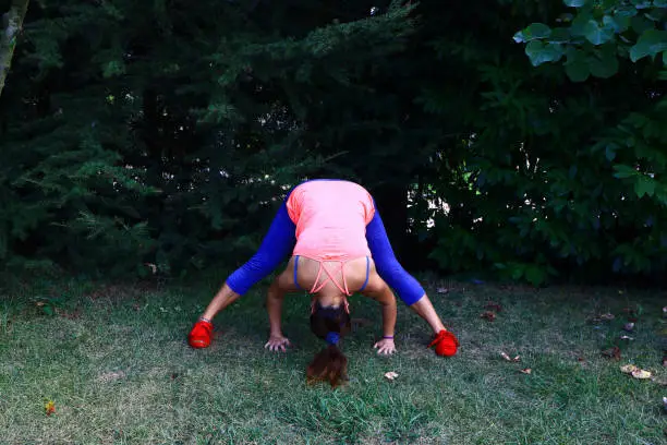 Yoga instructor shows prasarita padottanasana, wide stance forward bend pose on green grasses.