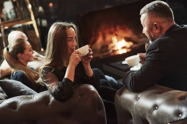 Drinks hot tea. Conversation between young and older generation. Family friends have nice evening near the fireplace in luxury modern restaurant